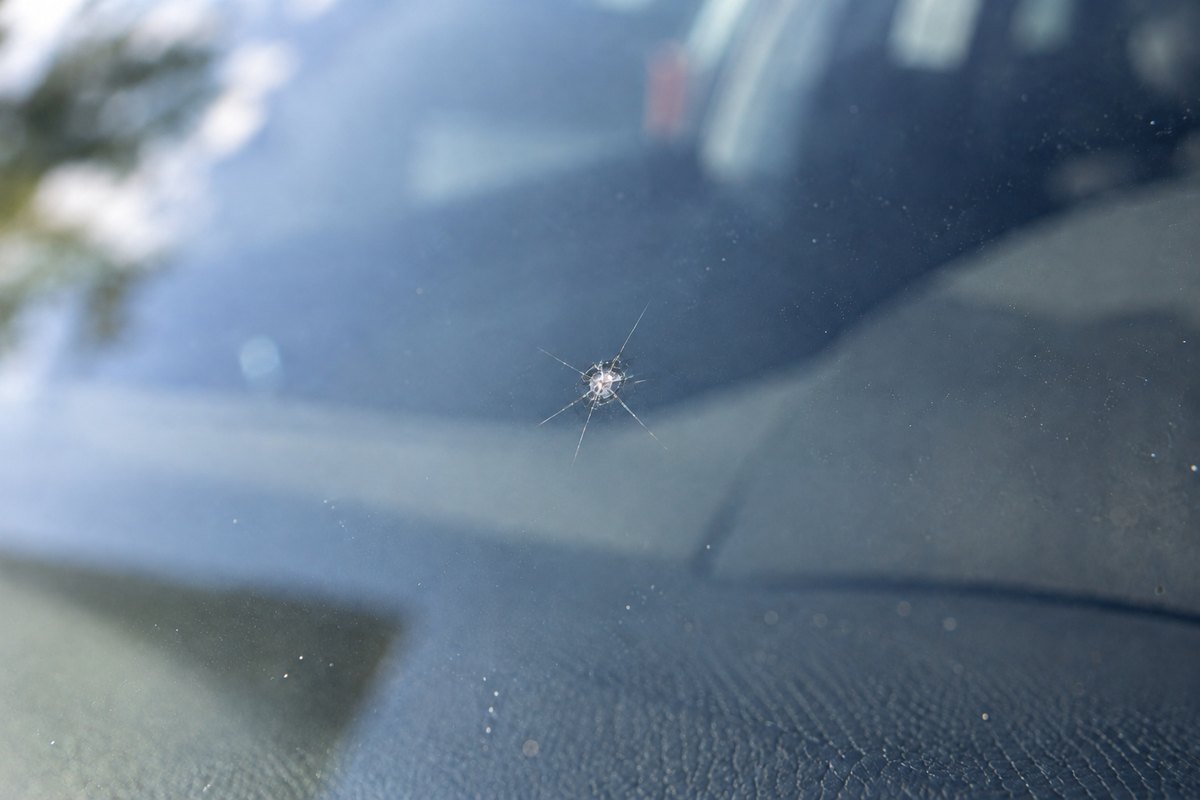 Close view of a small star-shaped rock chip in a windshield, a tiny impact pit with a few short cracks