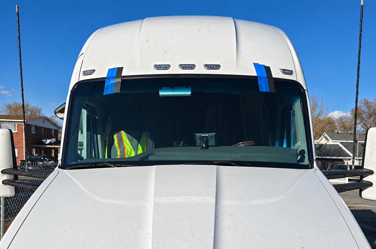 White semi truck cab with a newly fitted one-piece windshield taped at the top