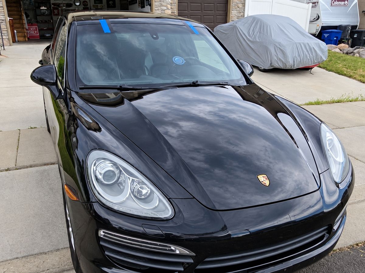Black Porsche SUV in a driveway with a newly fitted windshield held by blue tape